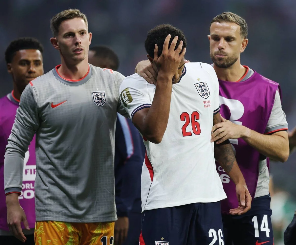 Soccer players in team jerseys stand on a field. One player is holding his head with his hand, possibly due to a foul or injury,